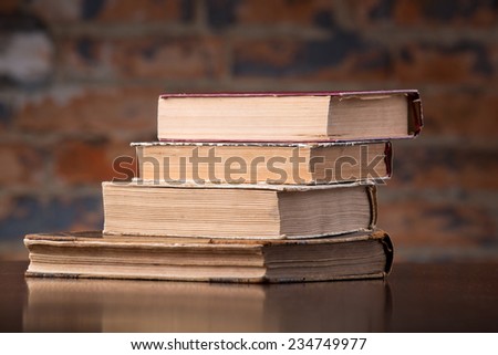 Vintage old books on a wooden table top  against a brick wall
