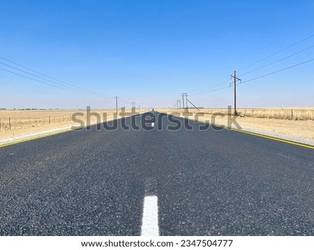 Low Centre of the fresh tar road picture featuring farmlands and power poles as a background
