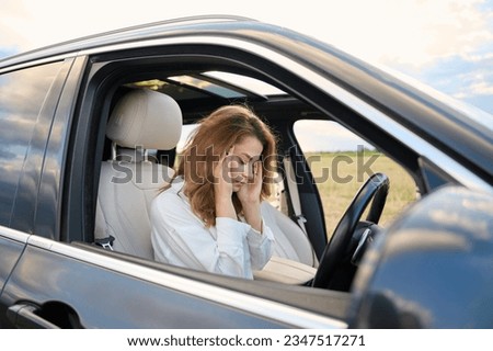 Close up image of young attractive woman with headache sitting behind the steering wheel holding her head. Migraine in a beautiful girl traveling by car. Driver's injury after an accident Royalty-Free Stock Photo #2347517271