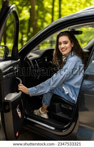 Portrait of gorgeous brunette in shirt entering her car. With one hand woman is holding steering wheel and with other shutting door. Royalty-Free Stock Photo #2347533321