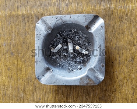 Addiction highlighted through burnt cigarette butt in ashtray with warning sign.
