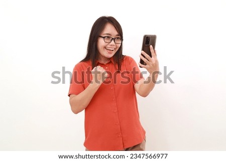 Happy succeed asian woman holding a cell phone while clenching her hand. Isolated on white