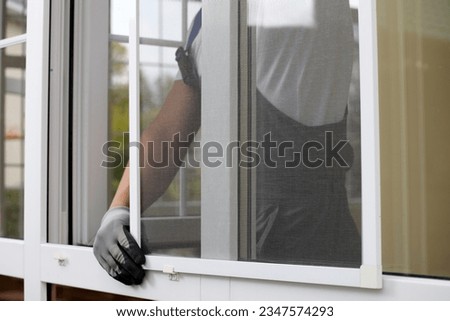 Close-up of the process of installing a mosquito net with the help of fasteners by a professional craftsman. Gloved worker inserts a white insect repellent grid into special brackets Royalty-Free Stock Photo #2347574293