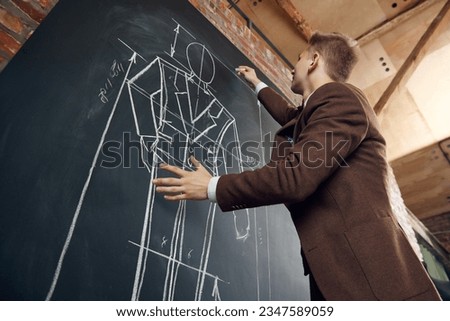 Bottom view of young man, fashion designer creating new collection of clothes, drawing suit sketches on blackboard. Concept of fashion, profession, creativity, occupation, hobby, business