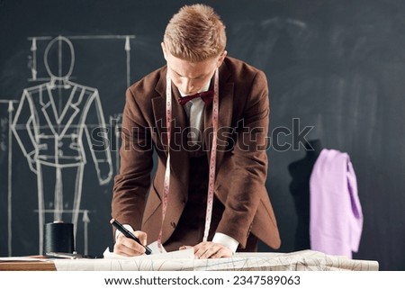 Young man, fashion designer in brown classical suit making sketches on tablet. Creating new clothing collection. Concept of fashion, profession, creativity, occupation, hobby, business