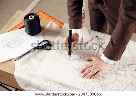 Top view of male hands, fashion designer making professional sketches on clothes on table. Creating new fashion collection. Concept of fashion, profession, creativity, occupation, hobby, business