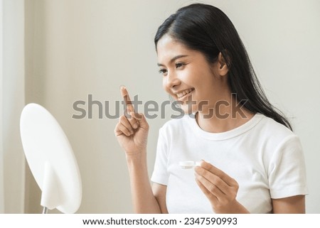 Ophthalmology care, eye sight, vision concept, happy asian young woman, female holding and putting soft contact lenses with finger on face from box case, looking in mirror at home. Medicine and health Royalty-Free Stock Photo #2347590993