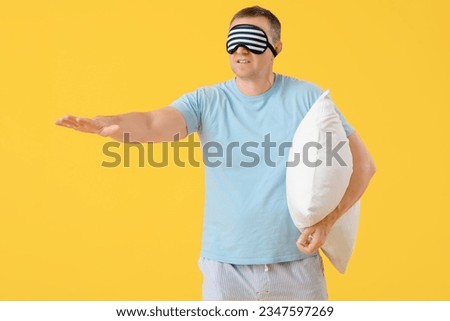 Mature man with sleeping mask and soft pillow on yellow background