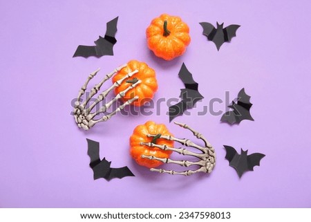 Composition with pumpkins, skeleton hands and paper bats on purple background. Halloween celebration concept