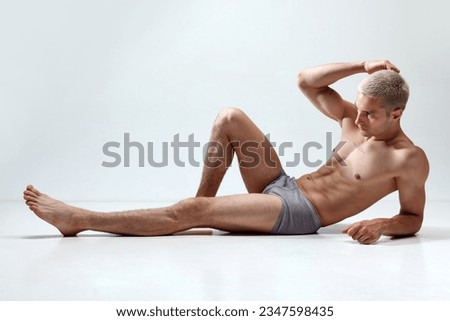 Young handsome man with muscular, relief, fit, strong body posing on floor in underwear against grey studio background. Concept of male natural beauty, body care, health, sport, fashion, ad Royalty-Free Stock Photo #2347598435
