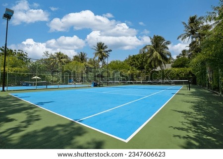 Amazing sport and recreational background. Blue tennis court on tropical landscape, palm trees and blue sky. Sports in tropic concept. Empty tennis court in summer sunrise sun light, outdoors. Royalty-Free Stock Photo #2347606623
