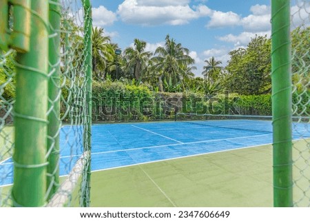 Amazing sport and recreational background. Blue tennis court on tropical landscape, palm trees and blue sky. Sports in tropic concept. Empty tennis court in summer sunrise sun light, outdoors.