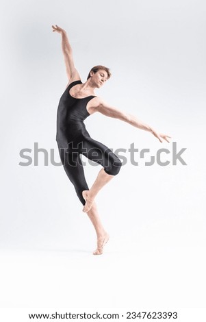 Contemporary Art Ballet of Young Caucasian Athletic Man in Black Suit Dancing in Studio Over White Background. Vertical image Composition