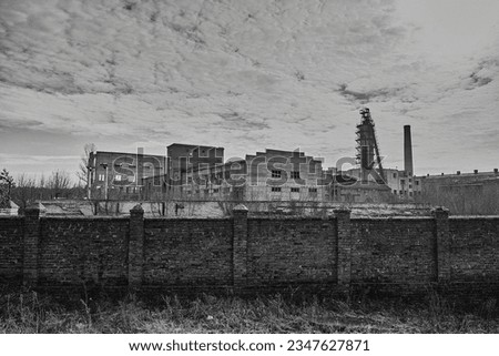 Behind the brick fence you can see an old, abandoned sugar factory, the sky matches the drama of the picture, black and white photography