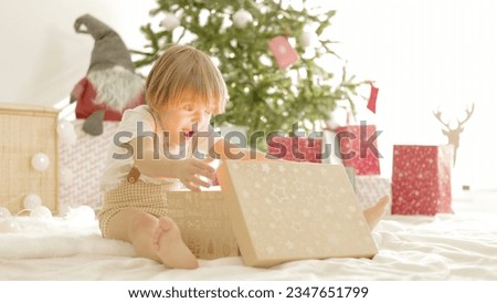 Little boy opening christmas presents with expression of happiness in the morning in the living room of his house.