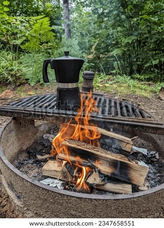 Black moka pot brewing on a fire pit in forest. Camping trip coffee brewing, morning in nature. Campfire burning