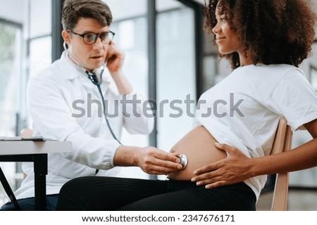 Pregnant african woman has appointment with doctor at clinic. Male gynaecologist OB GYN medic specialist with stethoscope listens to baby's heartbeat in mother's belly. Pregnancy, health care concept