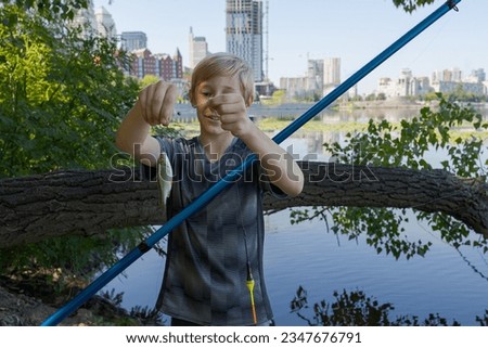 A teenager on a fishing trip shows off his catch - one small fish. Sport fishing on the river in summer.