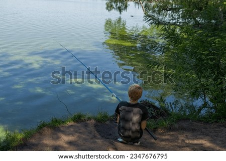 A teenager with his back turned is fishing with a cast rod. Sport fishing on the river in summer.