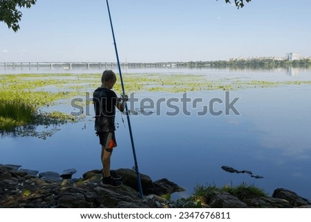 A boy holds a fishing rod in his hands and prepares to fish. Sport fishing on the river in summer.
