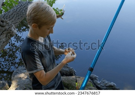 The teen angler checks the bait and puts a new one on. Sport fishing on the river in summer. Royalty-Free Stock Photo #2347676817