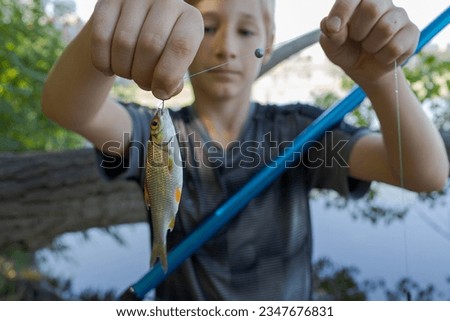 The boy shows Fishy's catch hanging on his hook. Sport fishing on the river in summer.