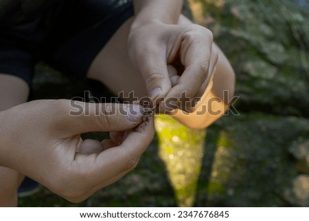 The hands of a teenager trying to put worms on a hook for fishing. Sport fishing on the river in summer.