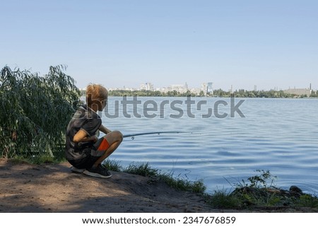 On the bank of a river, a boy is fishing while watching a float. Sport fishing on the river in summer.