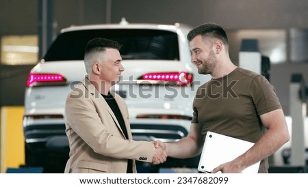 Handsome customer with car dealer agent making deal and signing on agreement document contract in car dealership. Successful middle-aged businessman is selling cars to male buyer in a car showroom