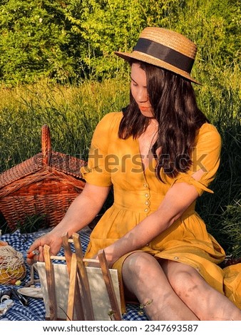 woman in a yellow dress and hat indulges in outdoor painting