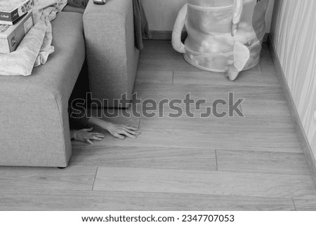black and white photo of children's hands, a child hiding under a sofa, playing hide and seek, in a nursery among toys