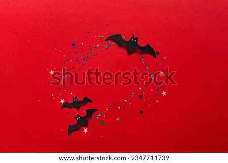Halloween decor concept. Blank greeting card, invitation mockup. Festive bright red background with glitter and sparkles, black paper bats. Copy space, flat lay, top view.