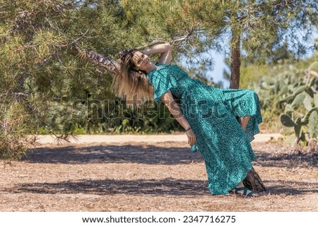 Cute blond girl with green dress leaning on a tree on a park.