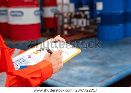 A worker is checking on the hazardous chemical material information form with background of chemical storage area at the factory place. Industrial safety working action. Selective focus. Royalty-Free Stock Photo #2347722917