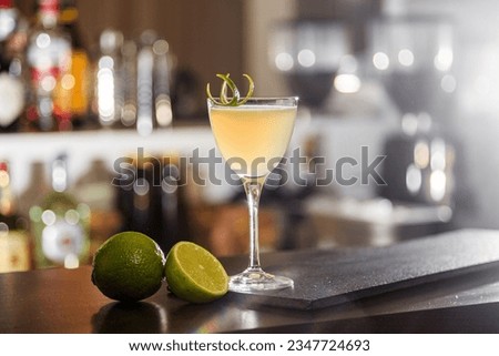 light beige cocktail on the bar against the background of blurred bottles in the bar