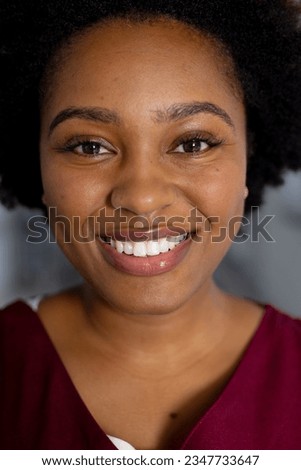Portrait of happy african american female doctor wearing scrubs in corridor at hospital. Hospital, medicine, healthcare and work, unaltered.