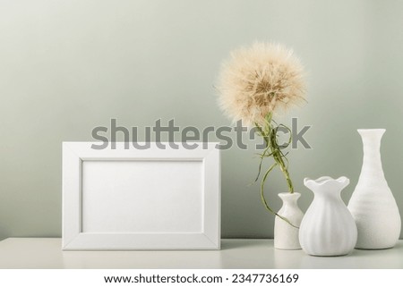 An empty photo frame and three white vases and a dandelion on the table.