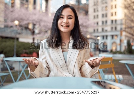 Young happy Asian business woman talking to camera outdoors having hybrid work meeting, online class, giving presentation or webinar, speaking during virtual event or shooting blog. Web cam view Royalty-Free Stock Photo #2347736237