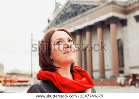 Positive young female woman 38 years old in red scarf looks up dreamily on classical building on street. dreams, wellbeing happy concept. close up portrait