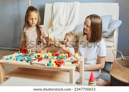 Babysitter's creative playtime. Learning through play and toys. Motherhood and family relationships. Smiling mother playing with little daughters engaged in game activity at home interior