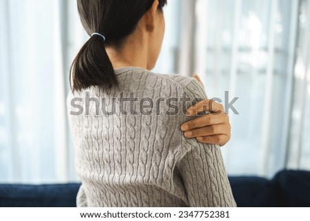 Young woman has problem with structural posture back neck and shoulder pain. Massaged her neck and shoulders for relief. reduce muscle tension on sofa couch in living room Royalty-Free Stock Photo #2347752381