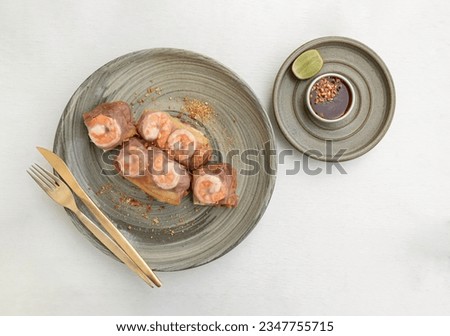 Homemade riceberry rice paper spring rolls stuffed with shrimp (prawn), sliced chicken, tofu, egg on ceramic plate served with sliced lime and chili sauce sprinkle with ground peanuts on white table.