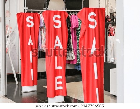 Red sale word banner at clothing store entrance. Seasonal discount offer in store