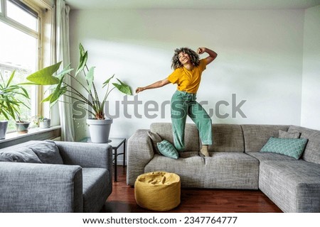 Happy afro american woman dancing on the sofa at home - Smiling girl enjoying day off lying on the couch - Healthy life style, good vibes people and new home concept Royalty-Free Stock Photo #2347764777
