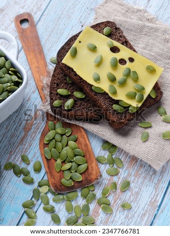 Pumpkin seeds. Still life for advertising photography for online store or marketplace. Peeled pumpkin seeds with gray bread and cheese lie on table. Top view. Useful breakfast.