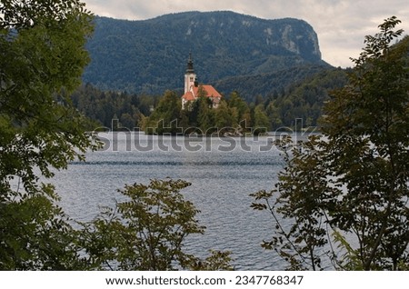 Scenic landscape view of Bled Lake with island and mountains in background. The most famous lake in Slovenia. Tree leaves border. Natural frame. Concept of landscape and nature.