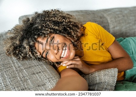 Happy afro american woman relaxing on the sofa at home - Smiling girl taking selfie picture with smartphone lying on the couch - Healthy life style, good vibes people and new home concept