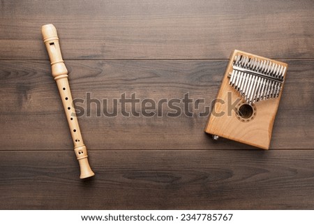 Overhead photo of block flute and kalimba with copy space. Flat lay top-down composition of wooden recorder and kalimba on the wooden background. Royalty-Free Stock Photo #2347785767