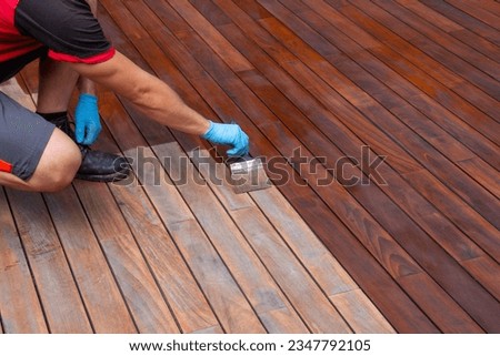 Worker applying terrace oil with a brush, wood decking renovation Royalty-Free Stock Photo #2347792105