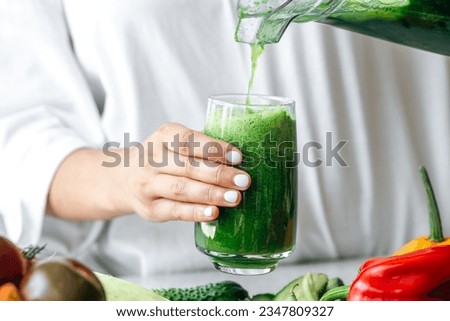 A woman pouring green smoothie to glass, healthy food concept. Royalty-Free Stock Photo #2347809327